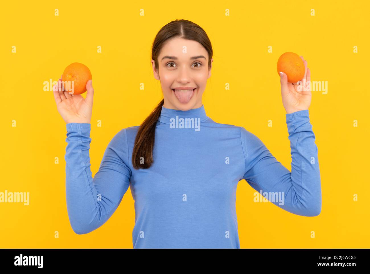 happy young woman holding orange citrus fruit on yellow background, organic Stock Photo