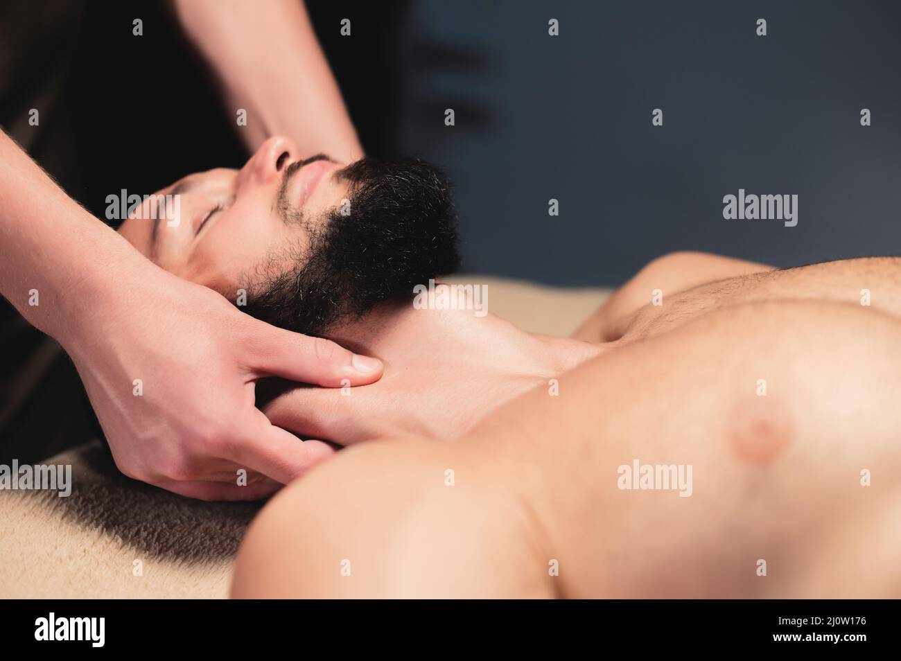 A male massage therapist makes a client athlete a man a neck massage in a dark cozy spa massage salon. Professional sports massa Stock Photo