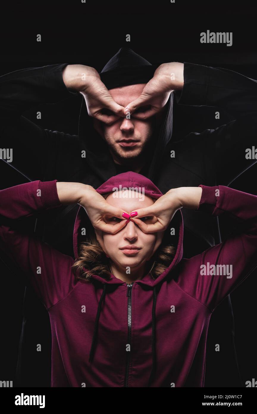 A low key pair of imaginary super heroes man and woman make gestures mask with hands. The hackers are among us. Couple in hoods Stock Photo