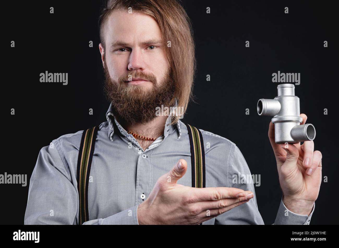 Portrait of a stylish bearded long-haired male salesman and dealer spare parts of the car in a shirt and suspenders. Holding a s Stock Photo