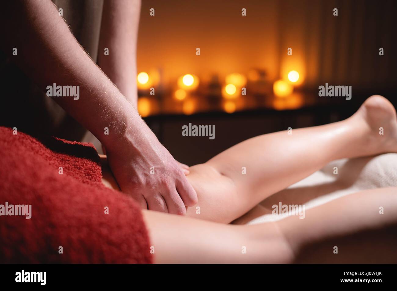 Close-up professional massage of the female hip in the dark room of the spa salon against the background of burning candles. The Stock Photo