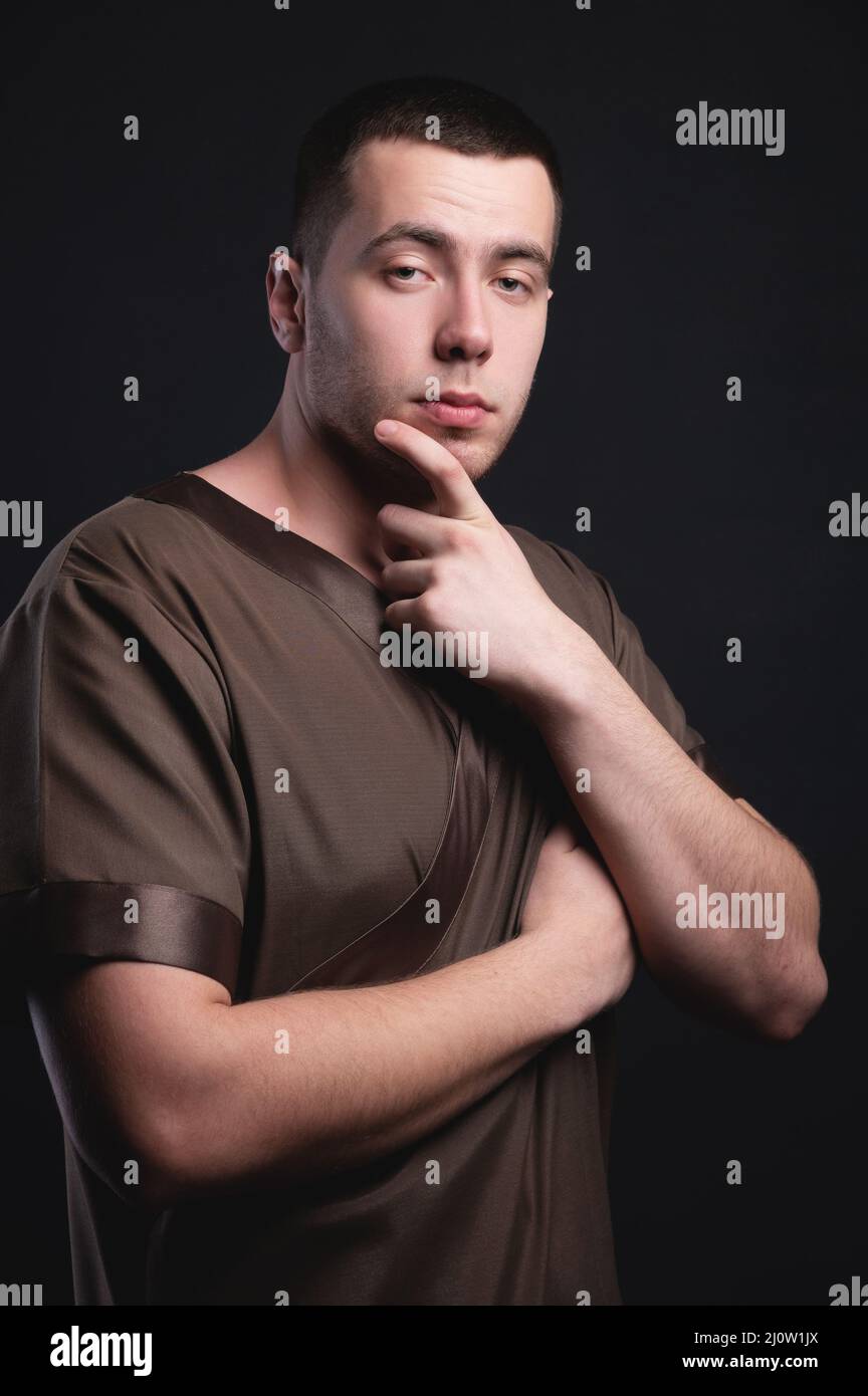 Portrait of a strong and large male masseur in special clothes with a finger at the temple reads your chin and knows all your di Stock Photo
