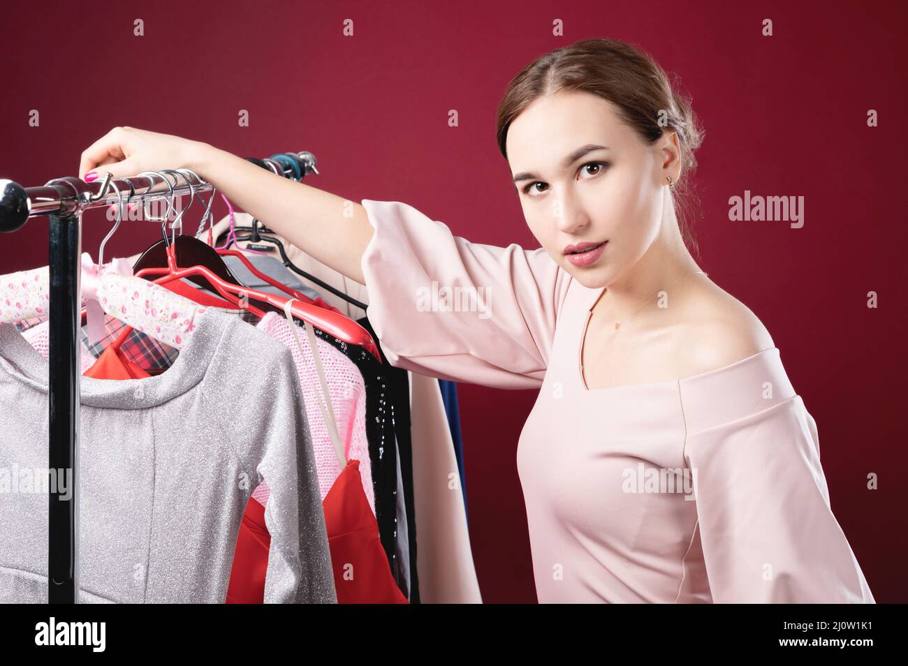 Serious perplexed standing next to a hanger for things holding one hanger in her hand. The concept of choosing clothes and happi Stock Photo