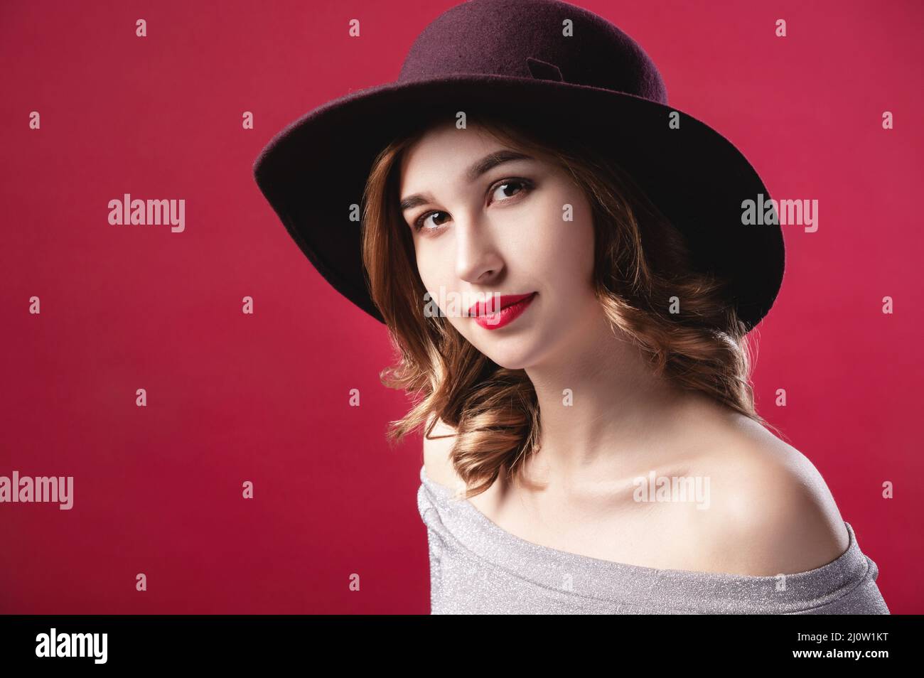 Fashionable attractive Caucasian girl in a large hat to large brim in a silver shiny dress on a red background. Studio retro por Stock Photo
