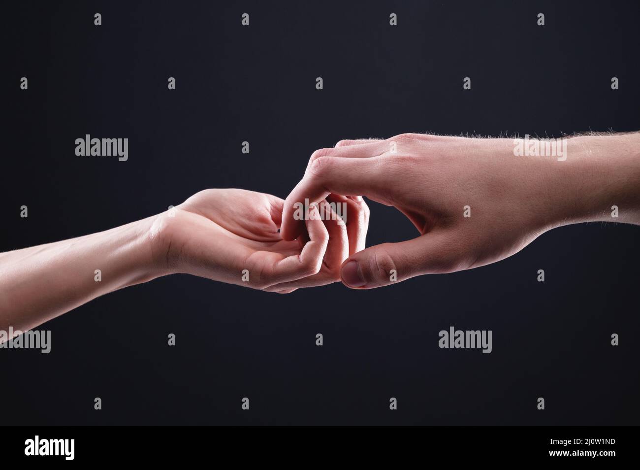 Two hands male and female ordinately hold each other symbolizing the help and mutual support between men and women on a black ba Stock Photo