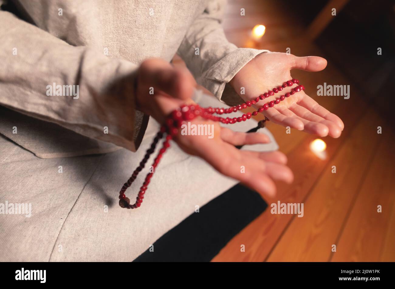 Close-up man in clothes for practice and meditation sits in a lotus pose and holds red rosary to concentrate attention in a wood Stock Photo