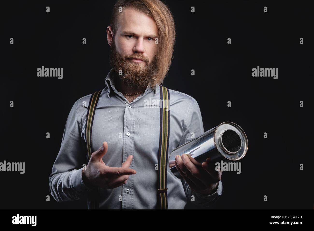 Portrait of a stylish bearded long-haired male salesman and dealer spare parts of the car in a shirt and suspenders. Holding a s Stock Photo