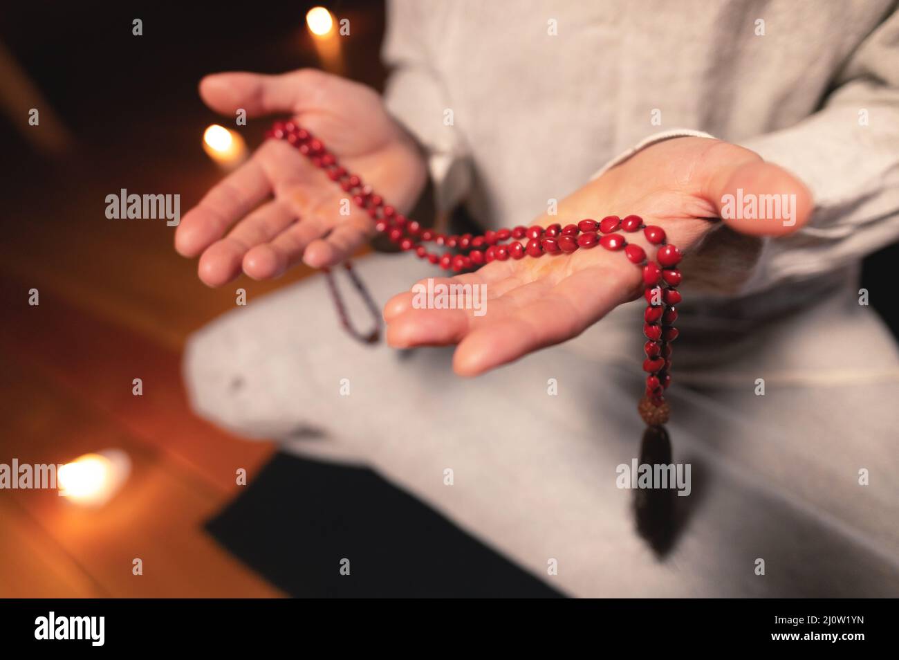 Close-up man in clothes for practice and meditation sits in a lotus pose and holds red rosary to concentrate attention in a wood Stock Photo