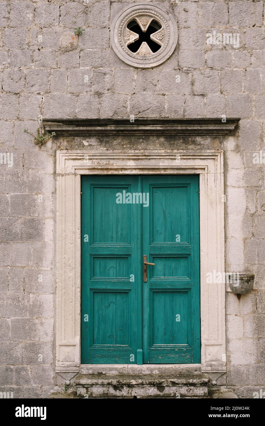 Green wooden door framed by stucco platbands with rosette window on top Stock Photo