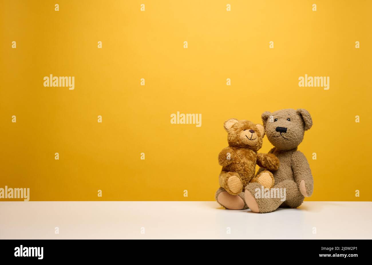 Two cute brown teddy bears sitting on a yellow background, childrens toy Stock Photo