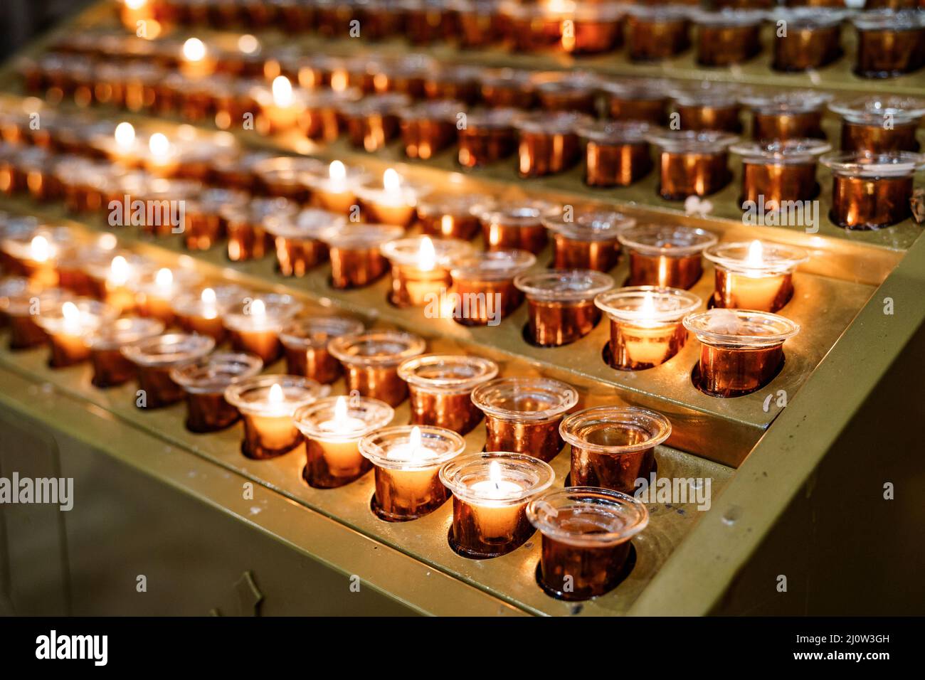 Votive candles burn in rows on a stand in the temple. Close-up Stock Photo