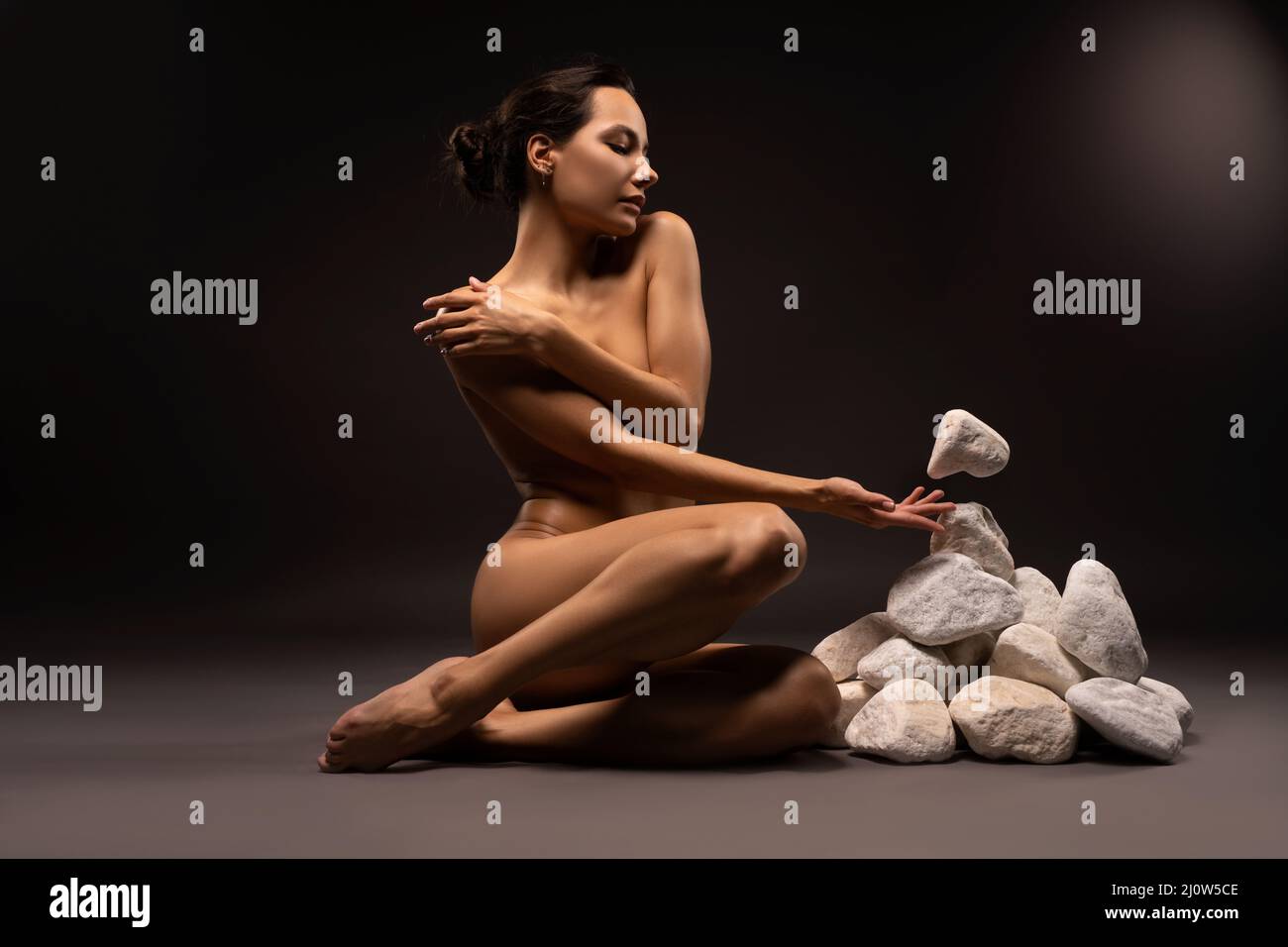 Naked slim woman near heap of levitating stones in studio Stock Photo