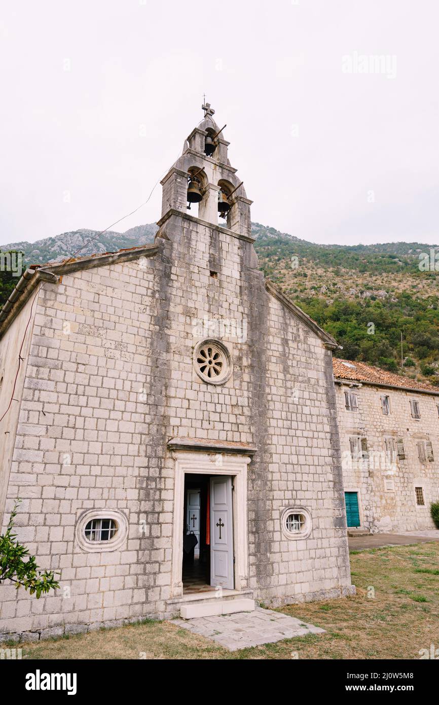Facade of an old stone bell tower with three bells in the background of mountains Stock Photo