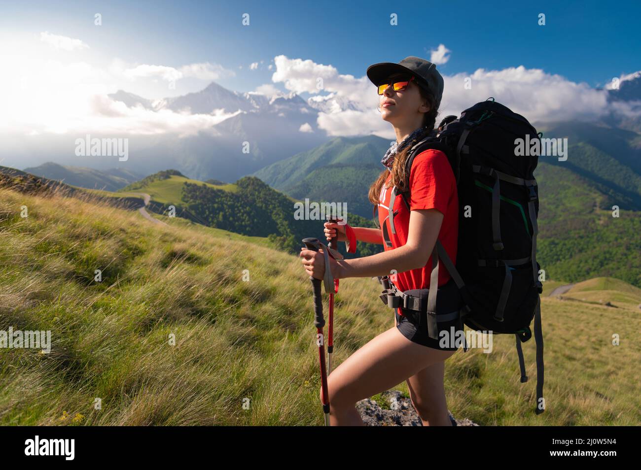 A tourist girl with a backpack admires the sunset from the mount Stock Photo