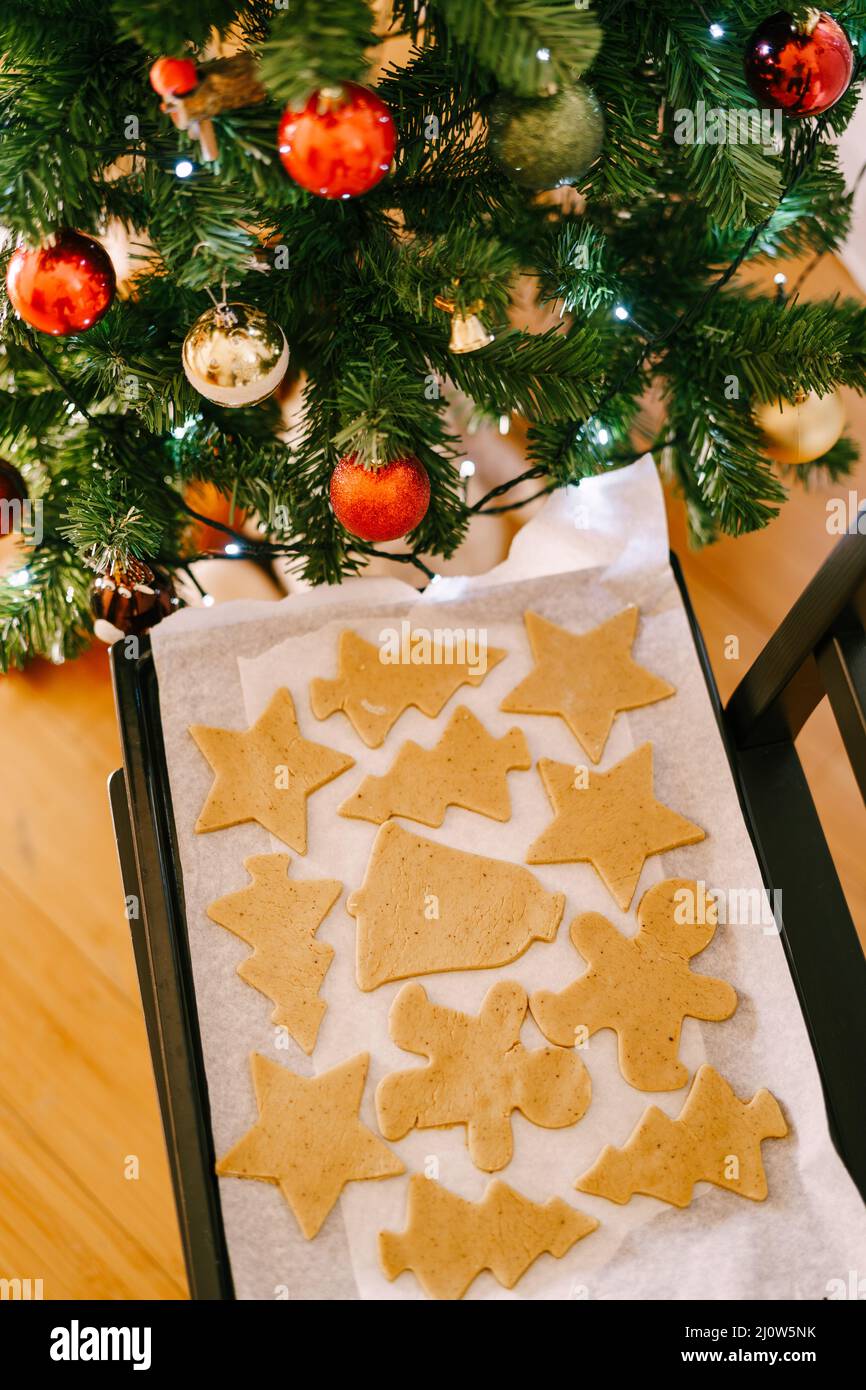Raw gingerbread on a baking sheet under a decorated Christmas tree. Stock Photo
