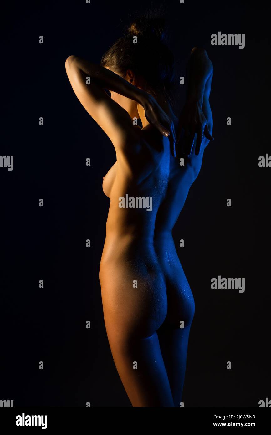 Nude woman gently touching back in dark studio Stock Photo