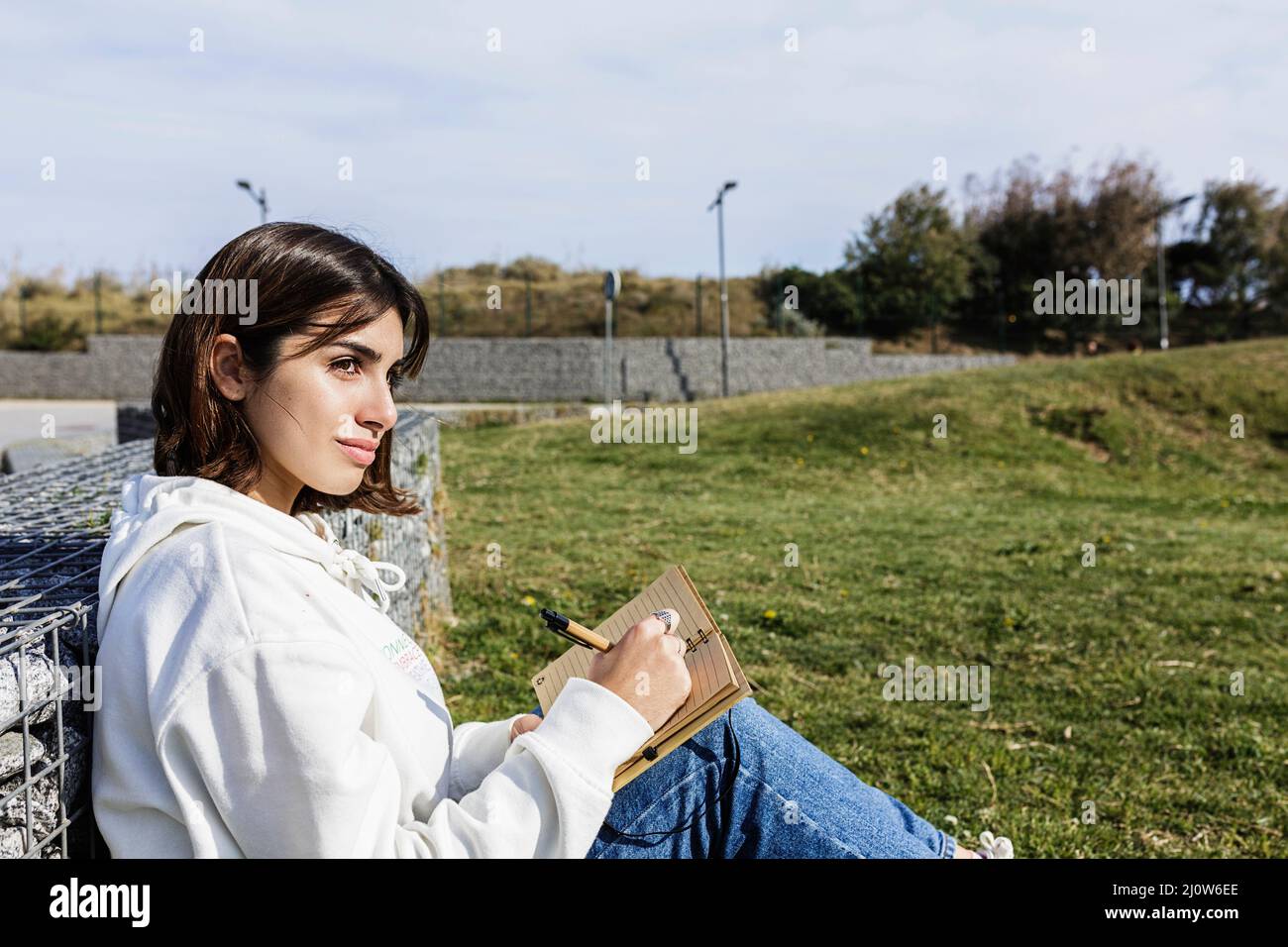 Young hispanic student writing in notebook while sitting in public park Stock Photo