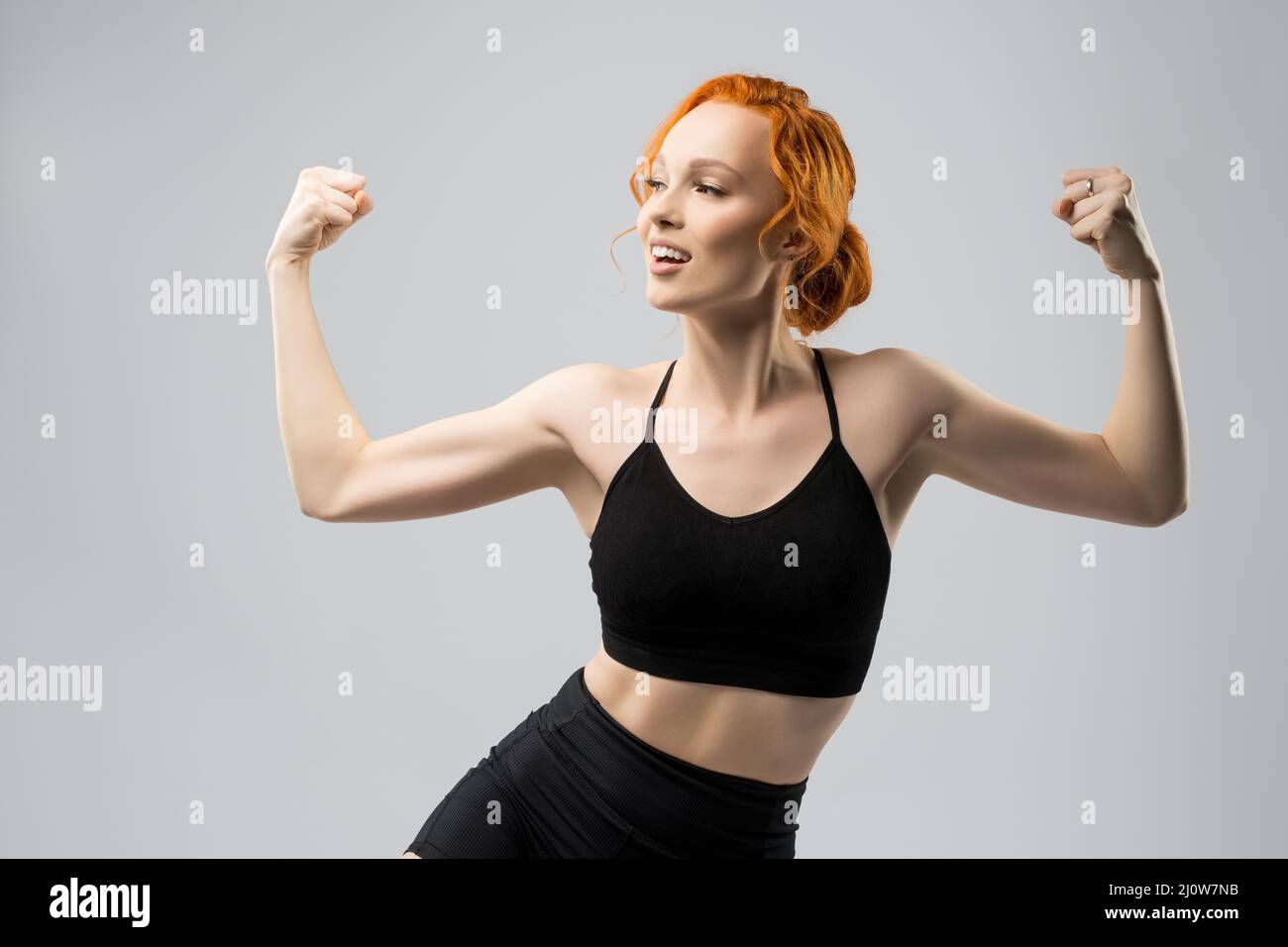 Positive young sportswoman showing biceps and smiling in studio Stock Photo
