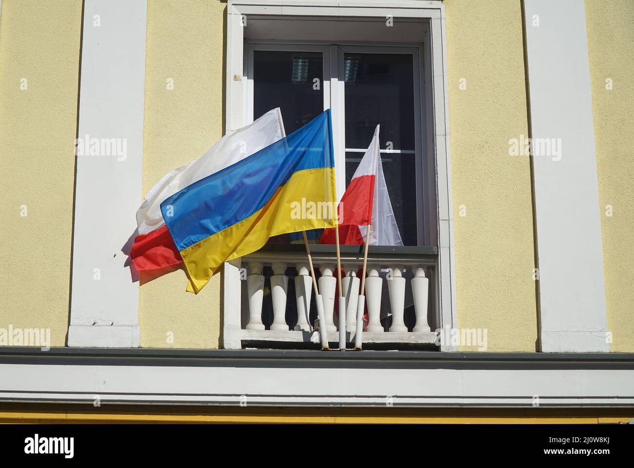 The national flags of Ukraine and Poland hangs in front of window as symbol of support Ukraine in Russian-Ukrainian war. Stock Photo