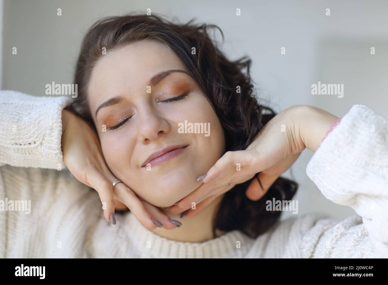 Close portrait of young happy pleased brunette girl with closed eyes touching clean fresh skin Stock Photo