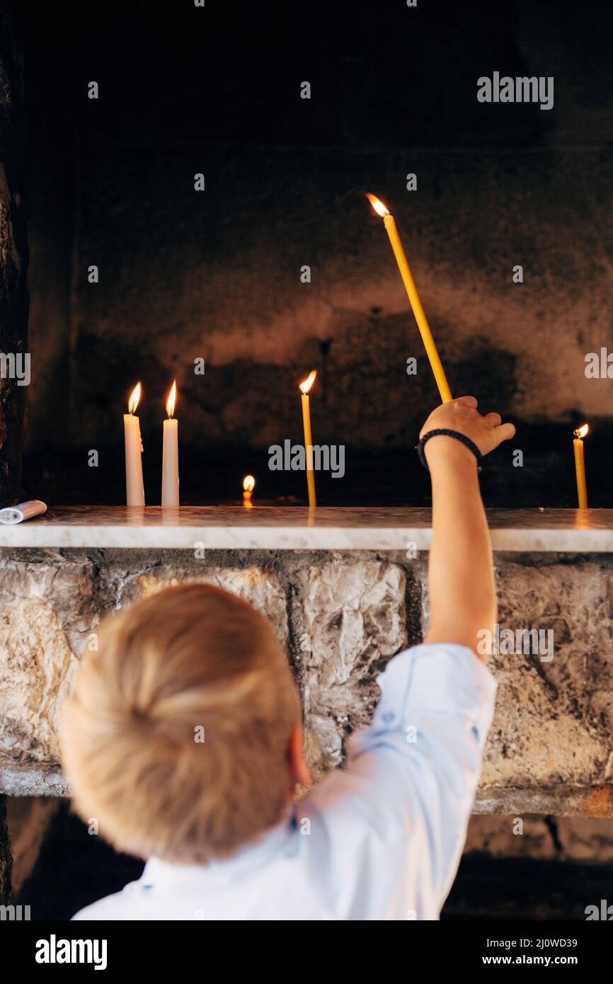 Boy puts a wax candle in a niche in a temple Stock Photo