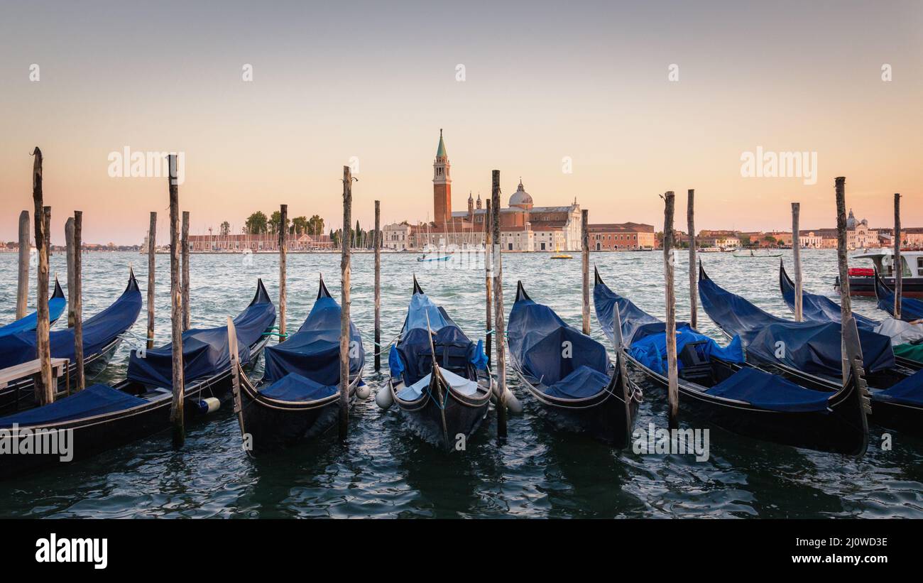 Gondolas moored docked on water in Venice. Gondoliers sailing San Marco basin waterway. San Giorgio Maggiore island with Campani Stock Photo