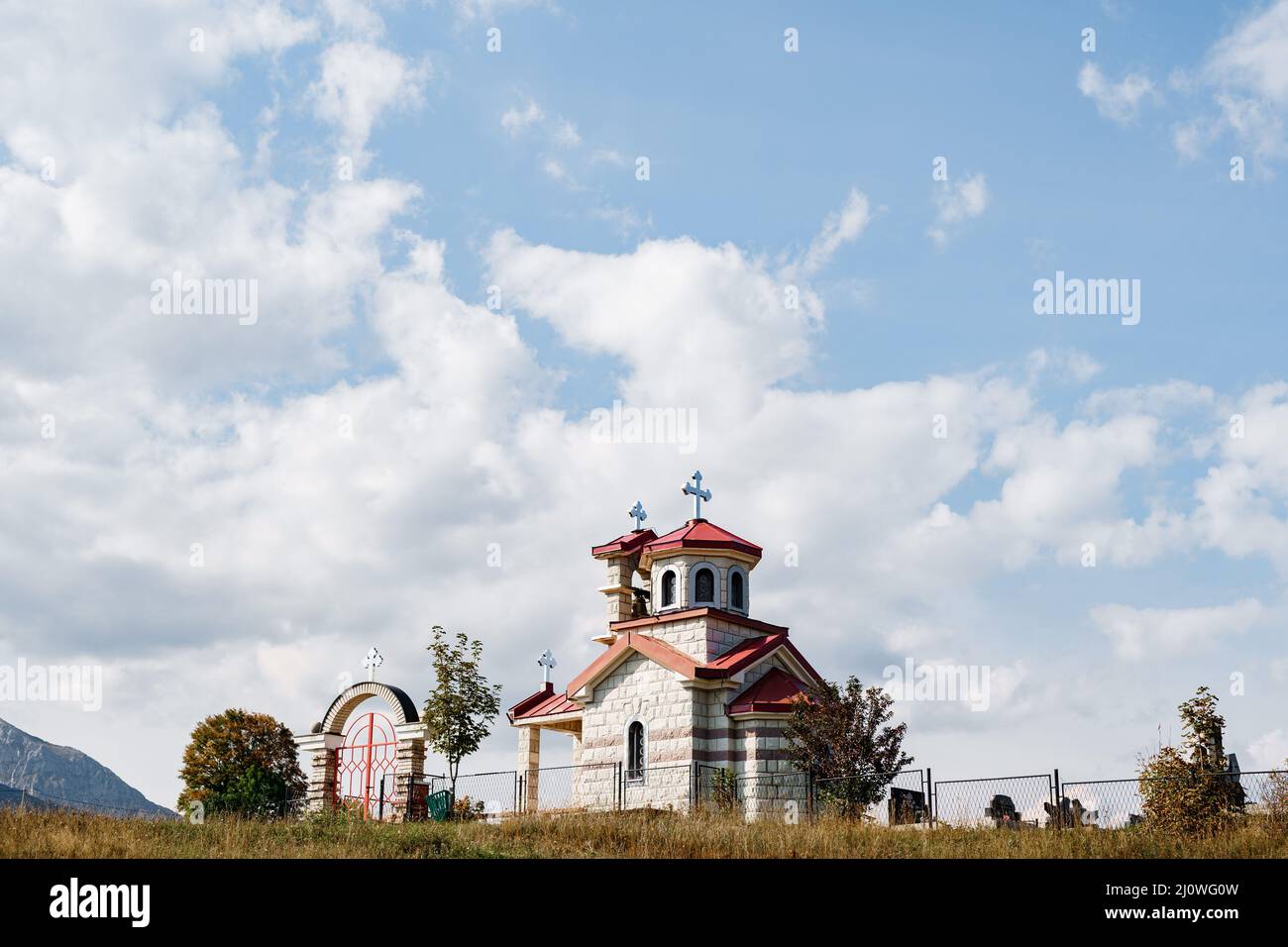 White brick church with a red roof in a field with a metal fence Stock Photo