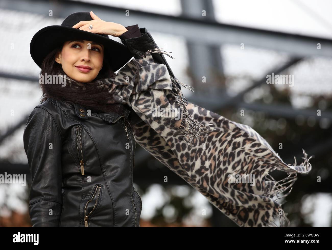 Beautiful fashionable woman holding her hat on a very windy day, scarf is flying in the air. Stock Photo