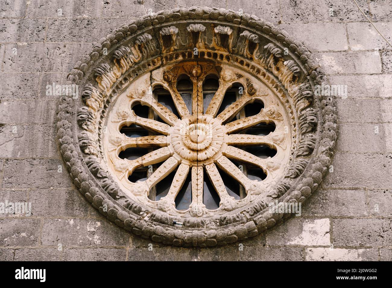 Rose window with ornaments and patterns on the dark stone wall of the church Stock Photo