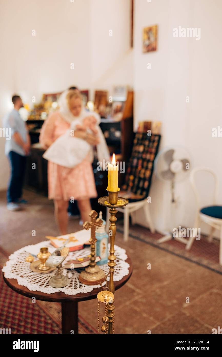 Burning wax candle on a high stand near the table with a cross and icons Stock Photo