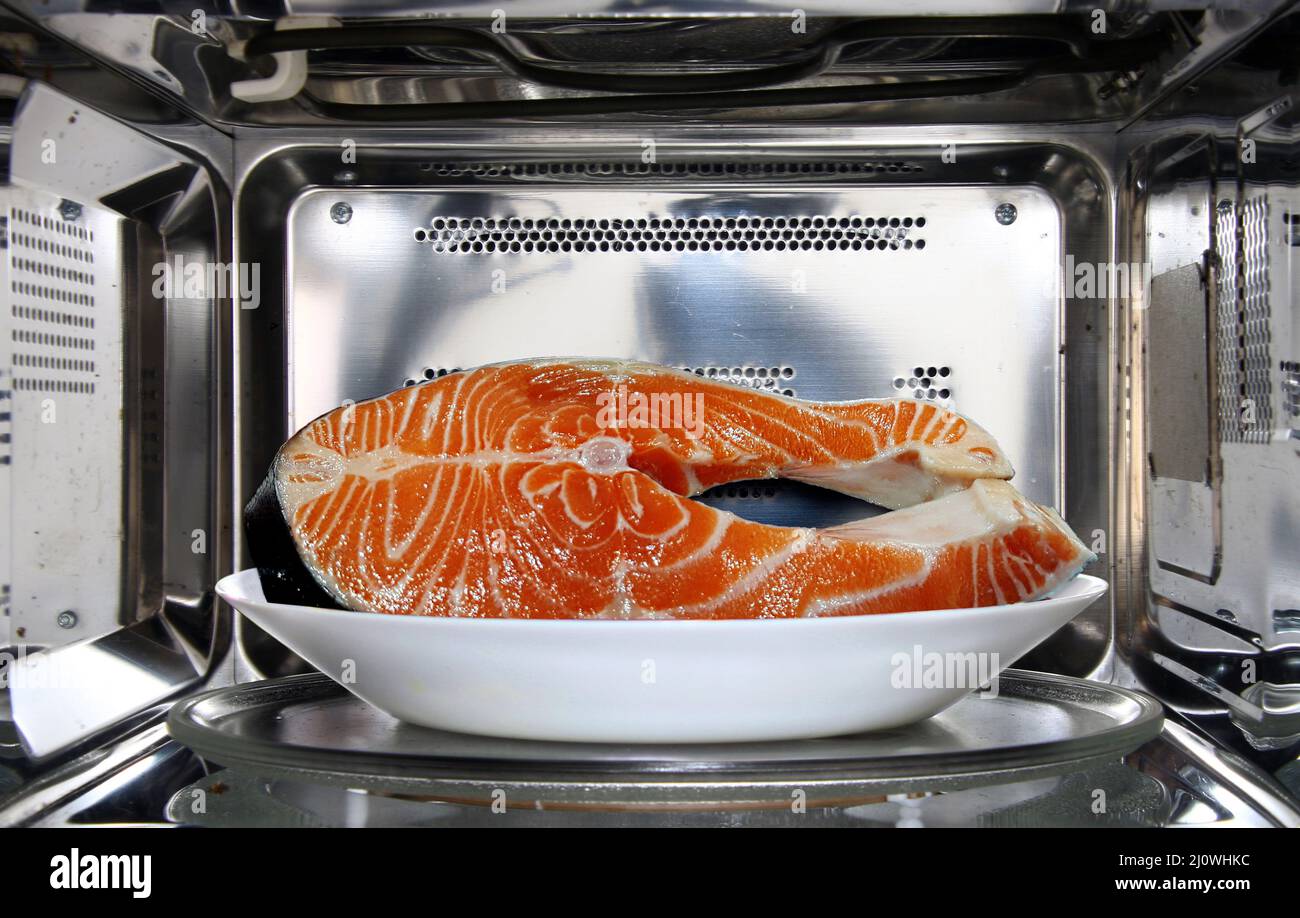 Raw fish in plate defrosting using microwave oven in close up Stock