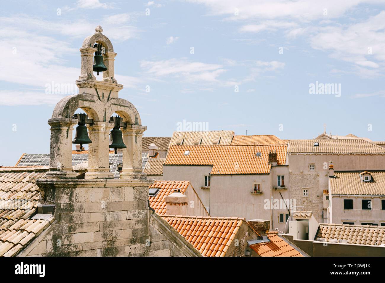 Three bells on an old stone bell tower among the tiled roofs of city buildings Stock Photo