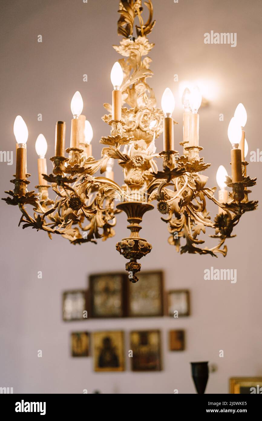 Gold chandelier with bulbs hanging in the church against the background of the wall with icons Stock Photo