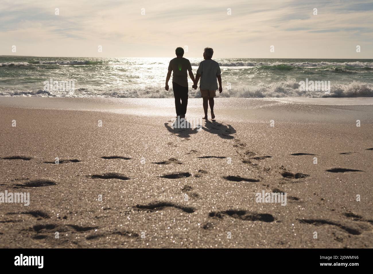 Full length of senior multiracial couple holding hands walking at beach ...