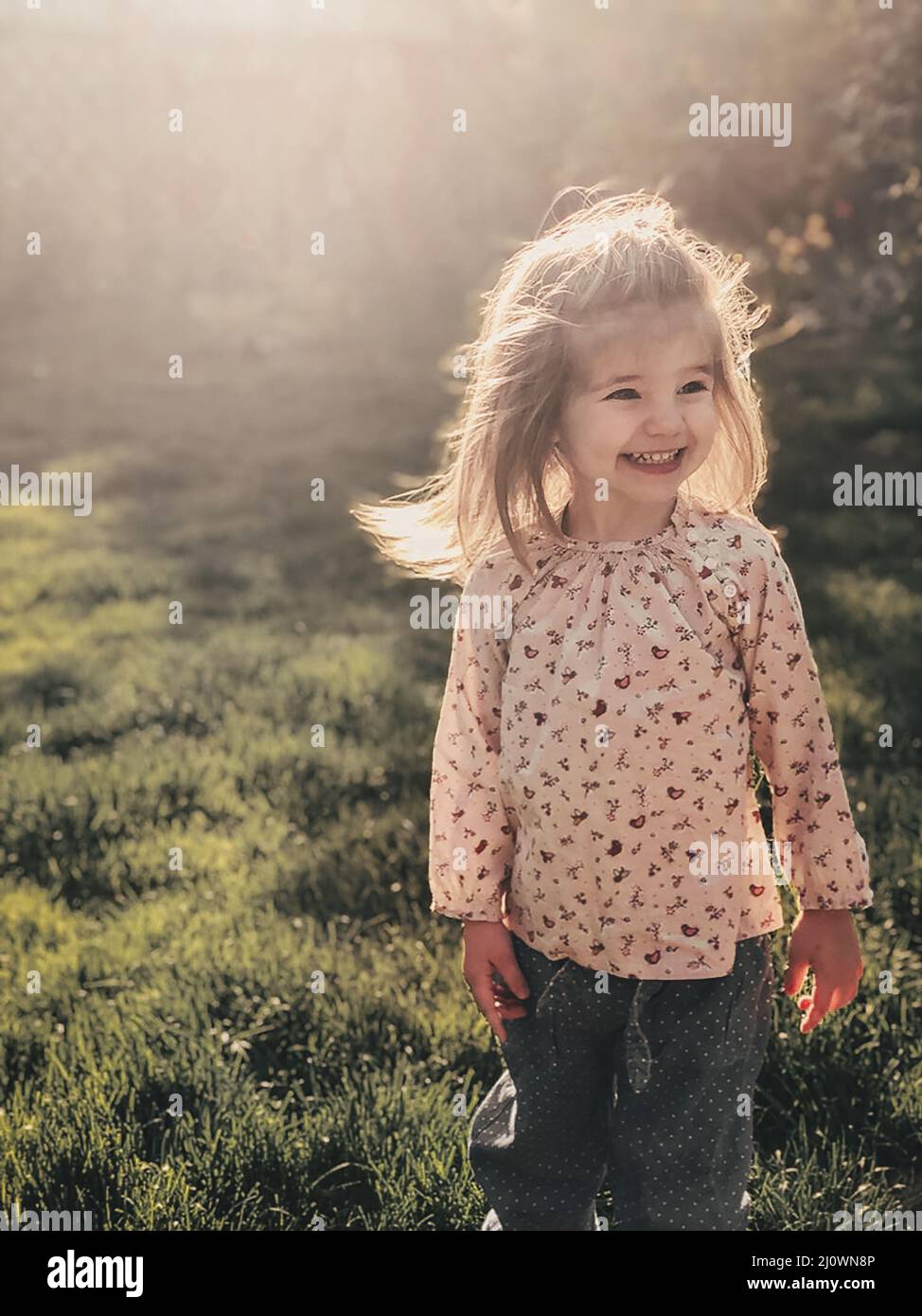 Close up photo of smiling cute little girl of 3-4 years old with blond fluffy hair stands outdoor Stock Photo