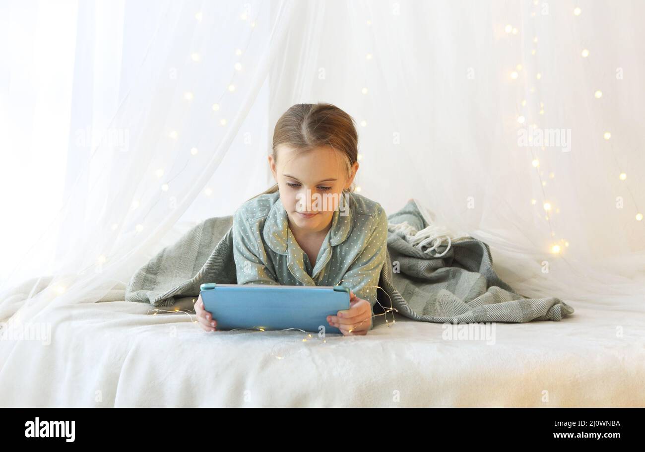 Little girl using digital tablet while lying on canopy princess bed ...
