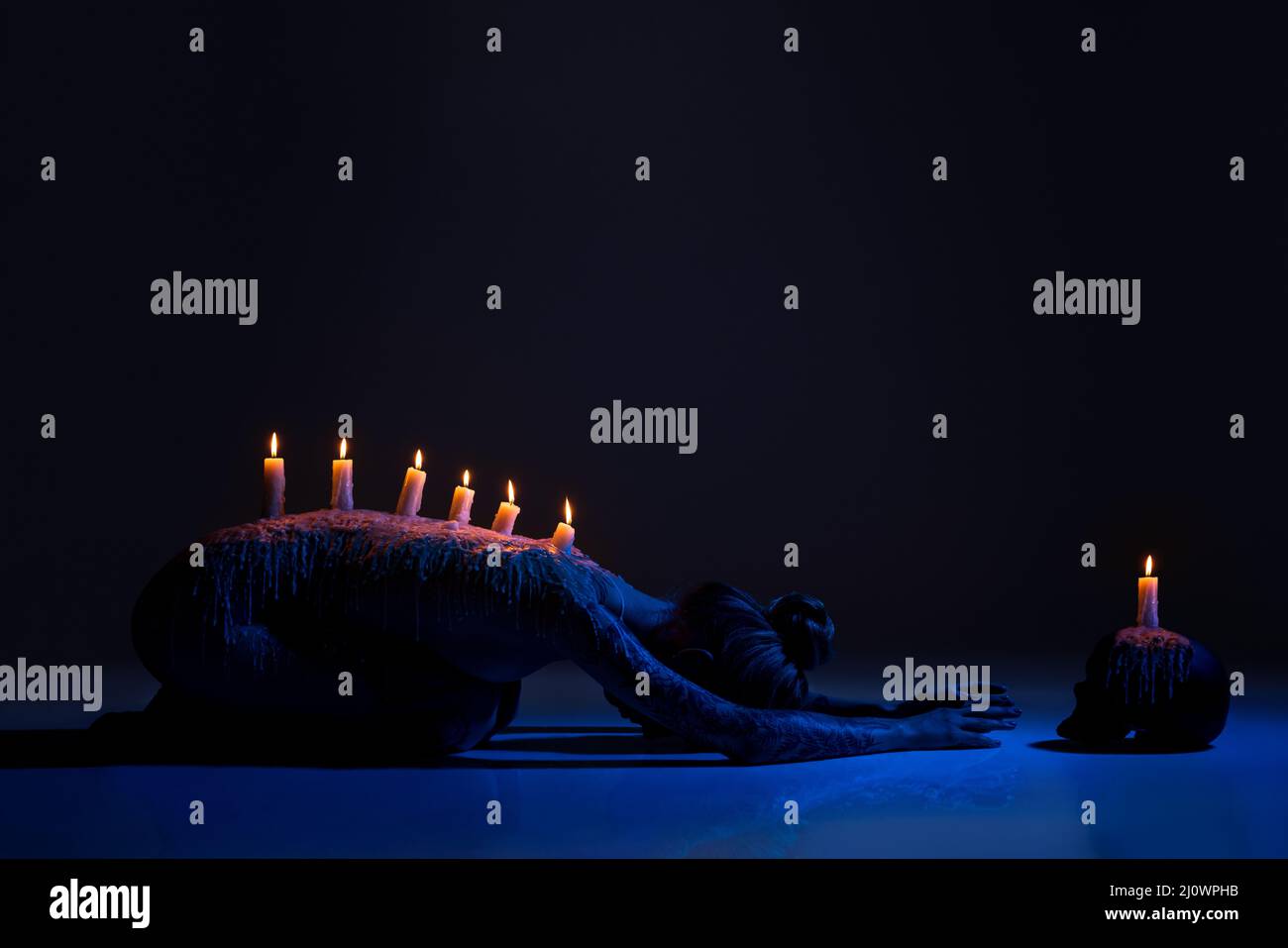 Burning candles on back of lady bowing down in darkness Stock Photo