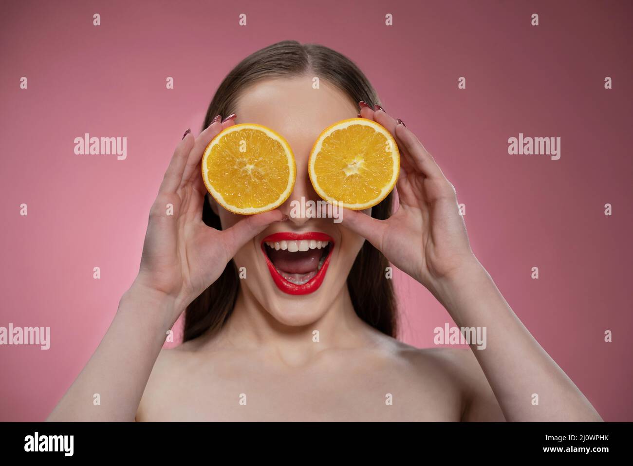 Funny beautiful beauty model young woman holding two juicy orange slices as her eyes or glasses. Charming joyful funny lady with Stock Photo