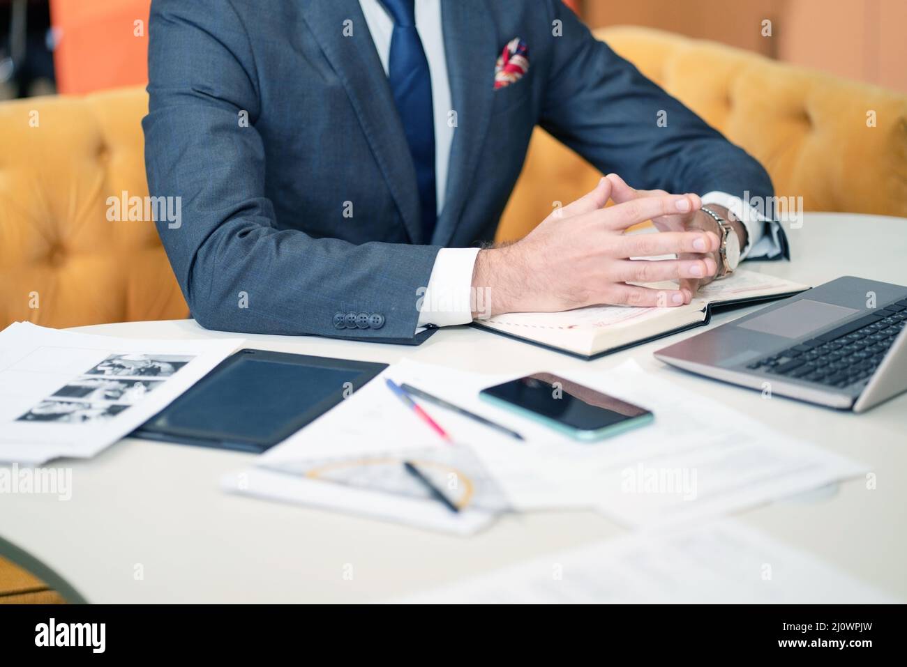 Torso of a Business Man in a Formal Suit, Sitting at his Desk, Hands are on the Diary. On the Table there is a Laptop, Work Pape Stock Photo
