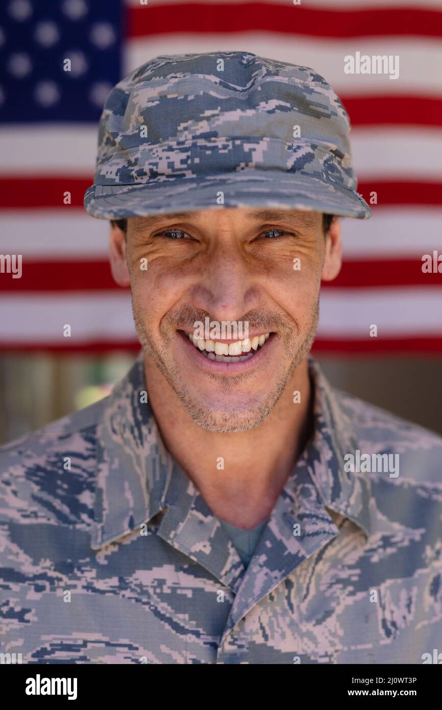 Portrait of smiling caucasian army soldier wearing cap and camouflage uniform against usa flag Stock Photo