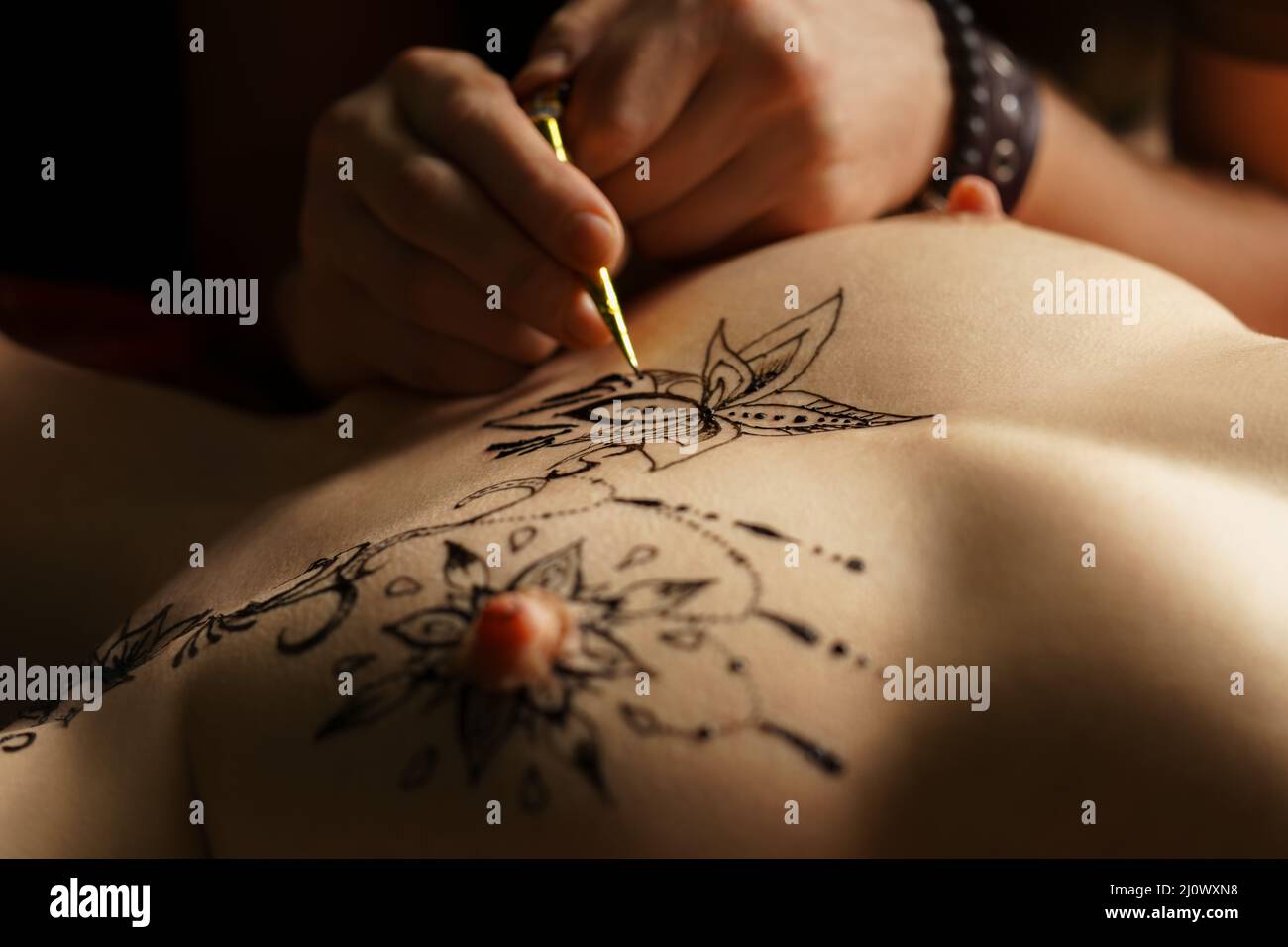 Artist applying henna tattoo on bare woman chest Stock Photo