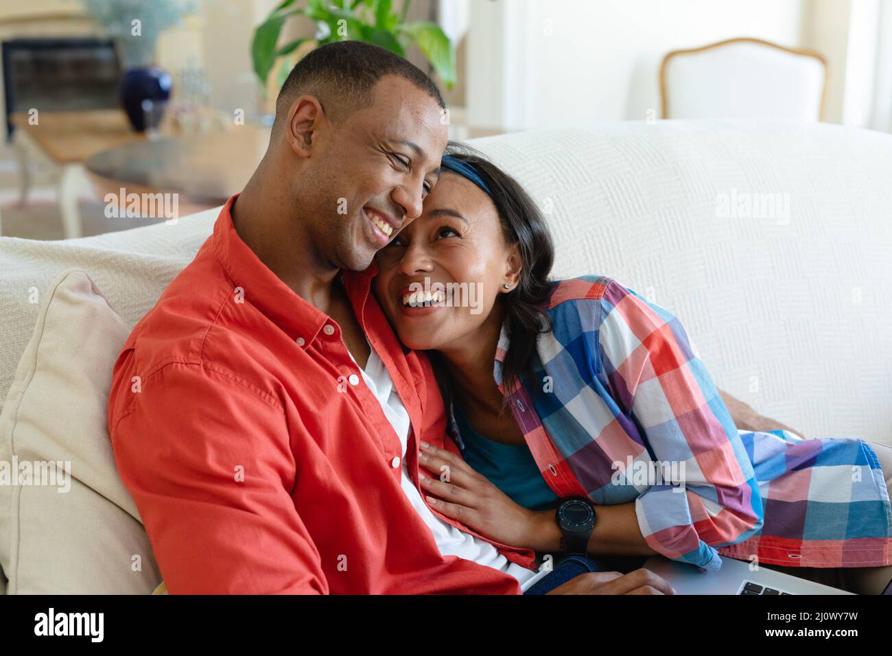Happy african american young couple lying with laptop on sofa at home ...