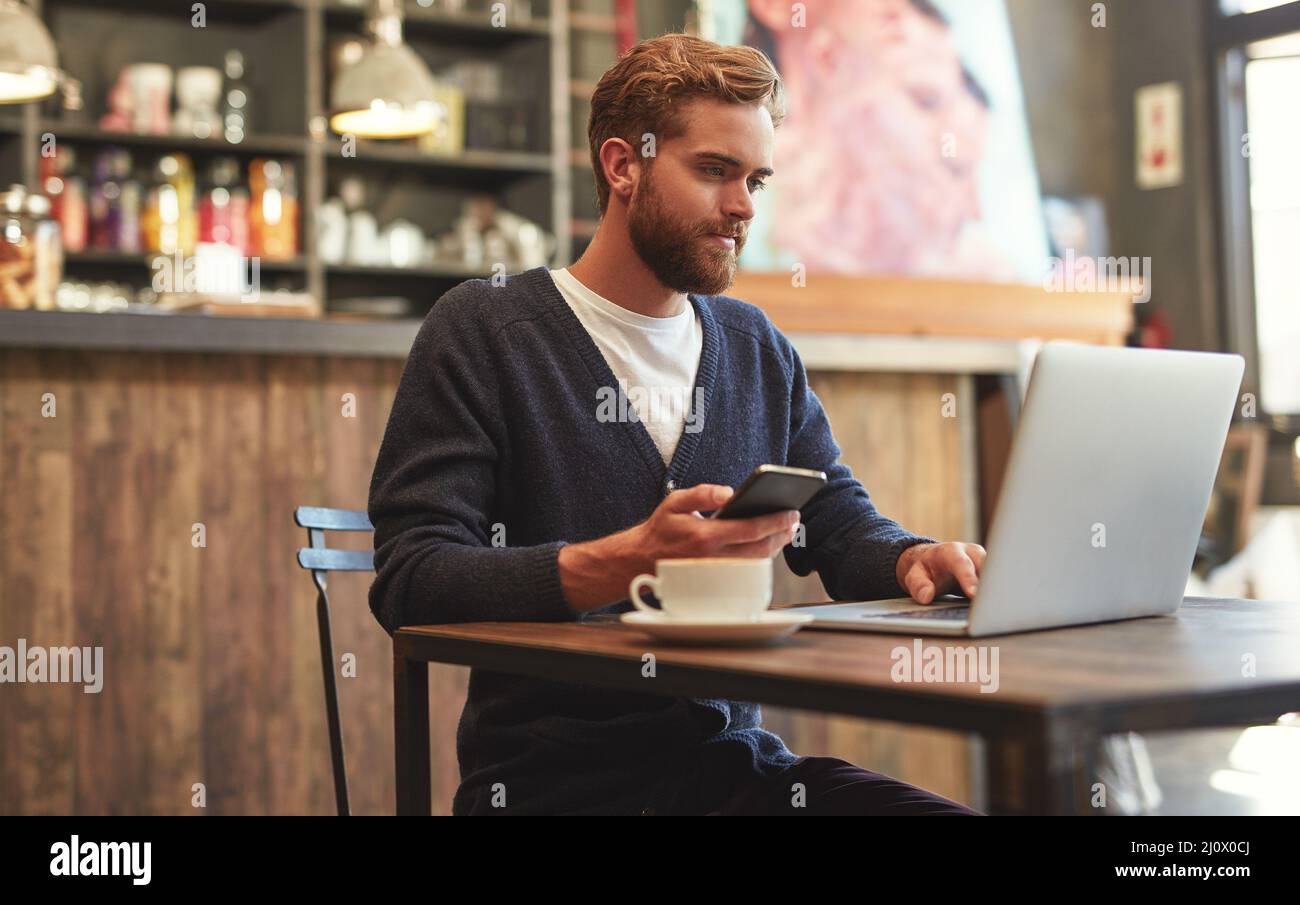 Technology gives him the freedom to work anywhere. Shot of a young man using a laptop and phone in a cafe. Stock Photo