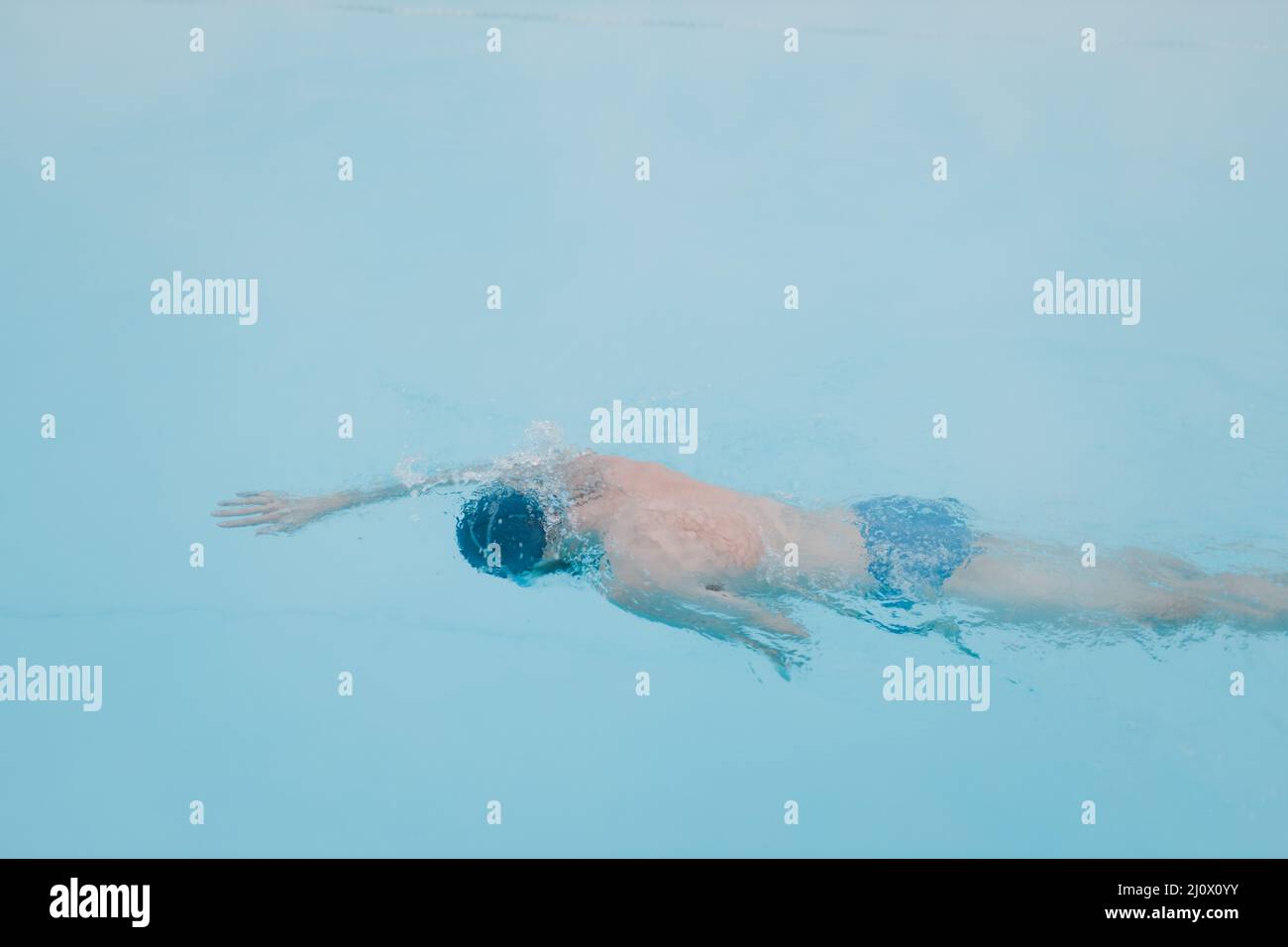 Fit swimmer male training swim in open winter swimming pool with fog. Geothermal outdoor spa concept, Stock Photo