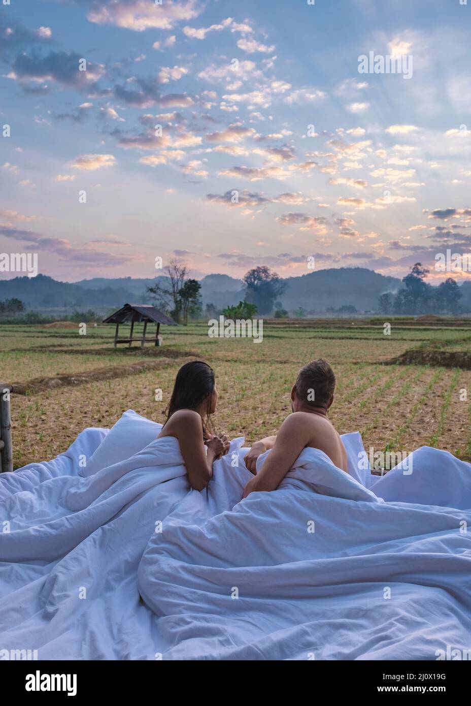Sunrise over rice paddies in Nan Thailand, man and woman in outdoor bed waking up with coffee in the morning in Thailand Nan Stock Photo