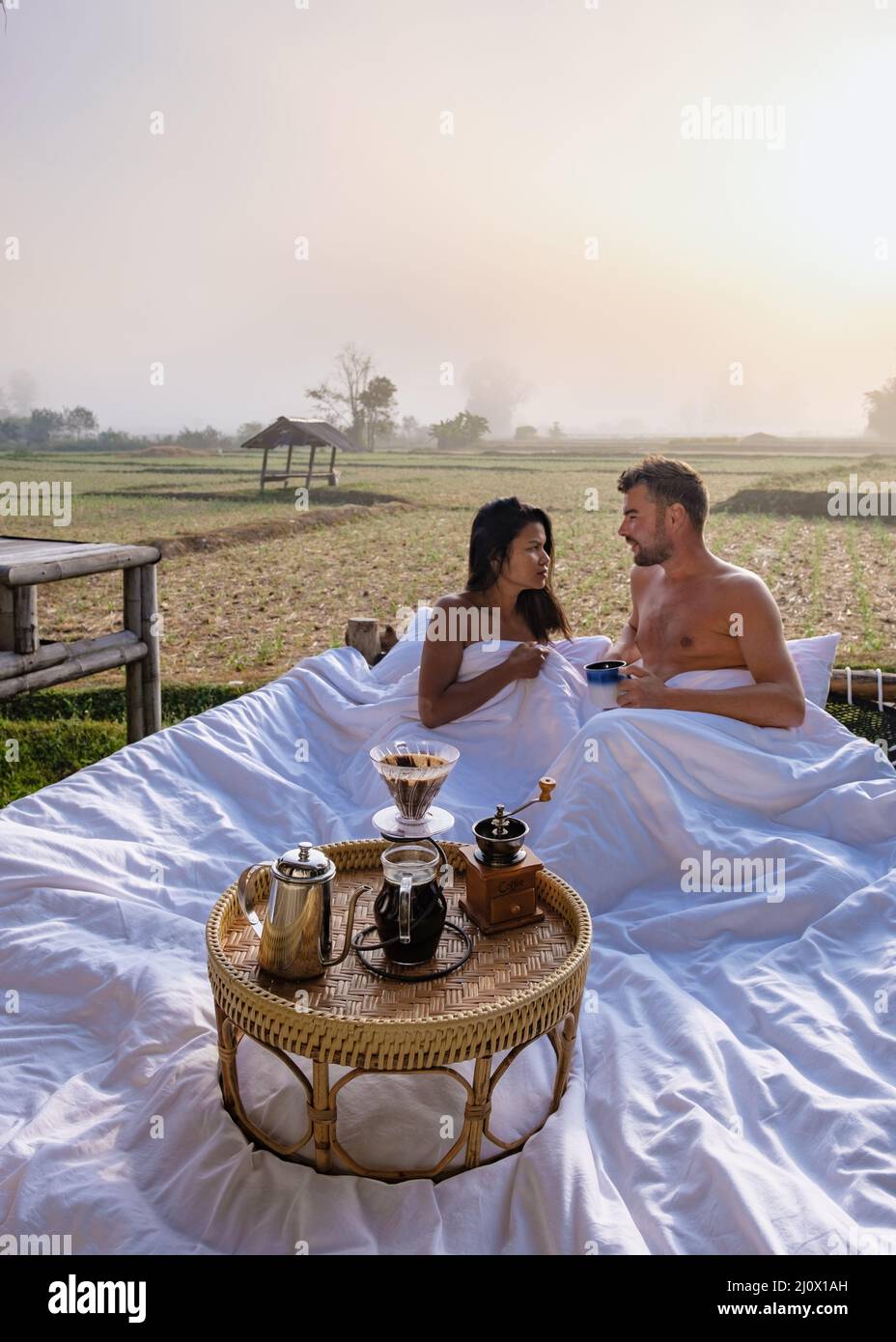 Sunrise over rice paddies in Nan Thailand, man and woman in outdoor bed waking up with coffee in the morning in Thailand Nan Stock Photo