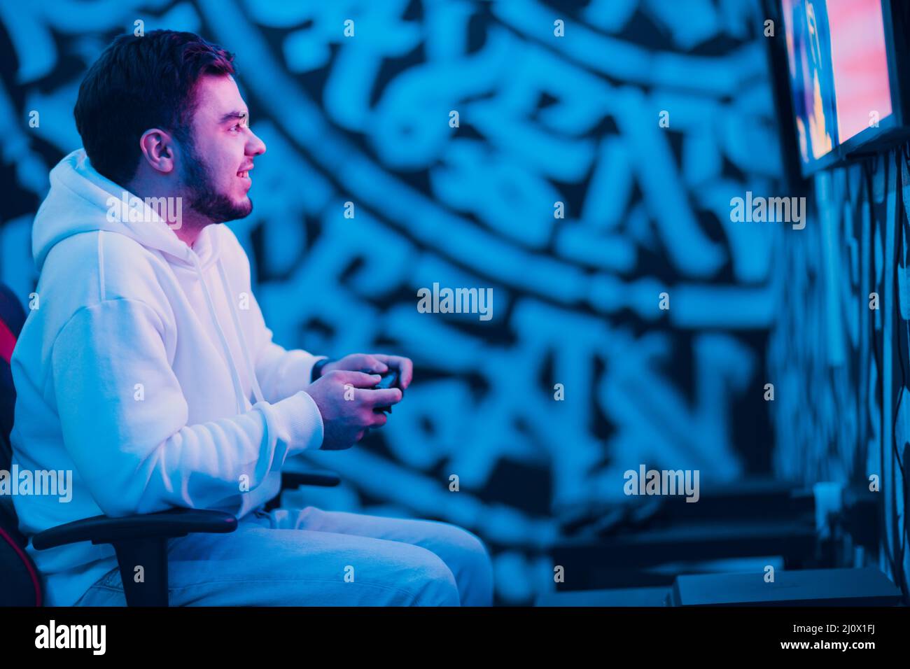 Young man plays on game console with gamepad sitting on chair Stock Photo