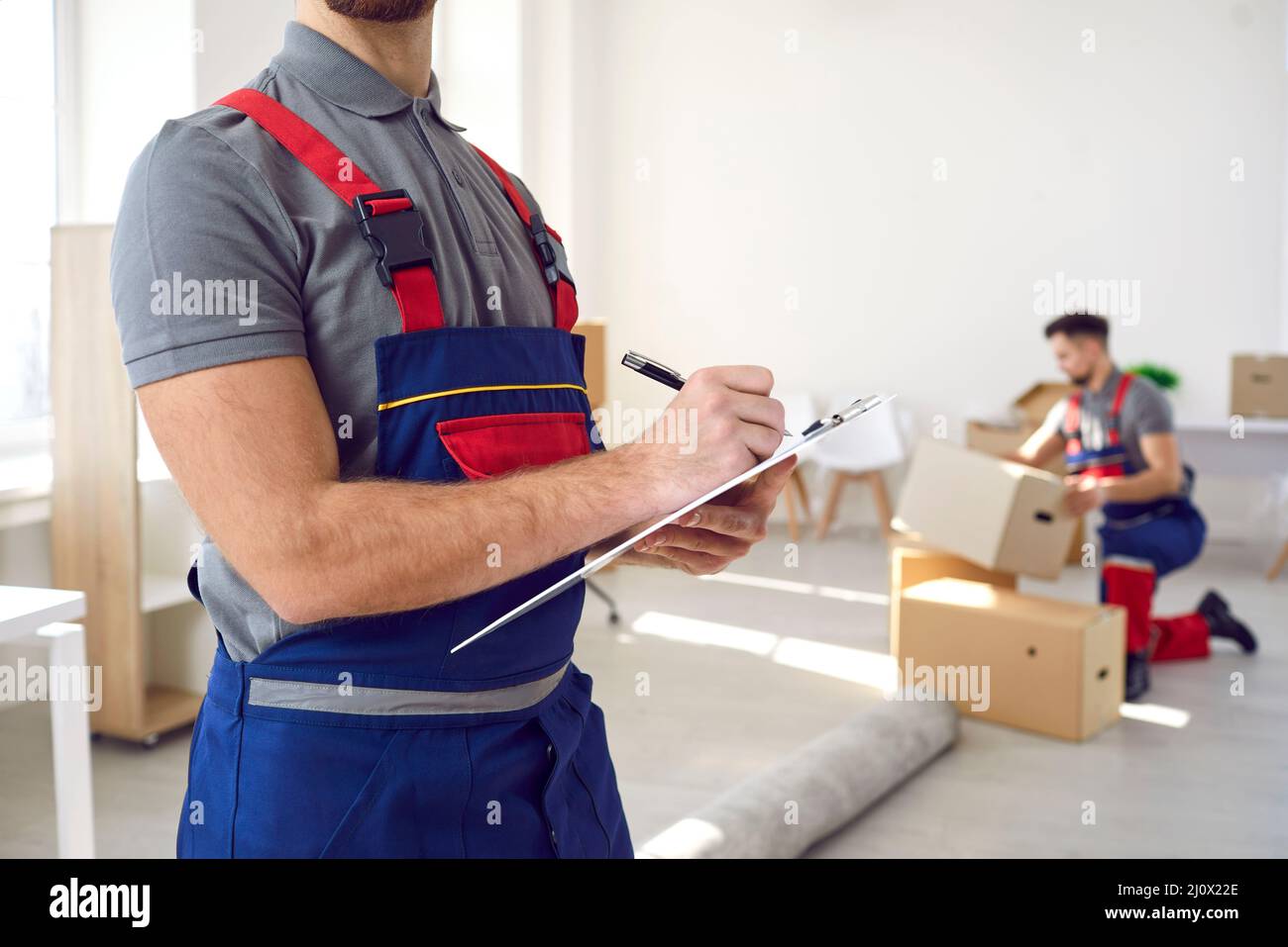 Male employee of moving company makes inventory of packed boxes and writes data to clipboard
