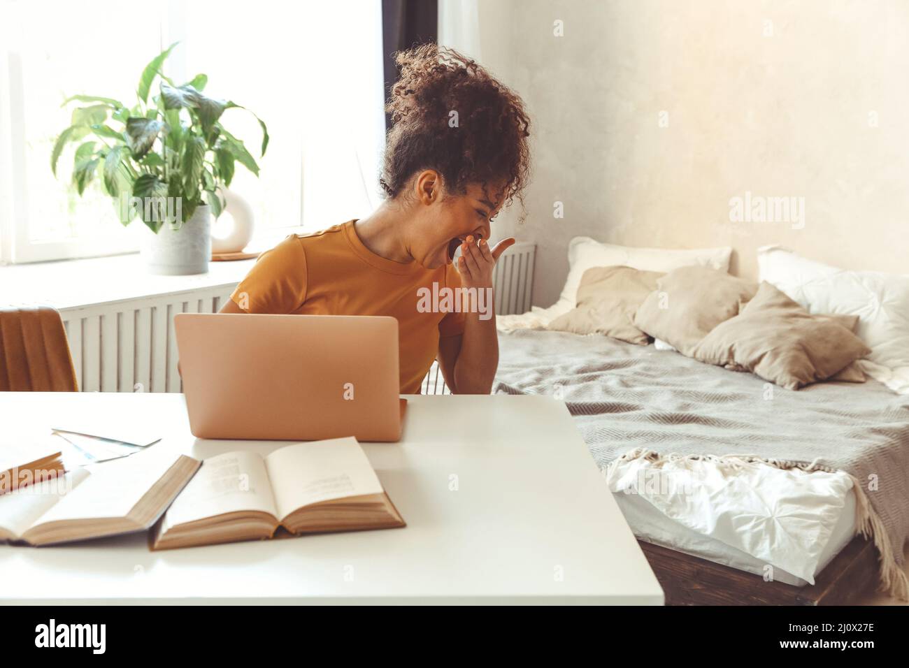 Tired flustrated African descent young girl sitting at desk in front of laptop while yawning cover mouth with hand not having in Stock Photo