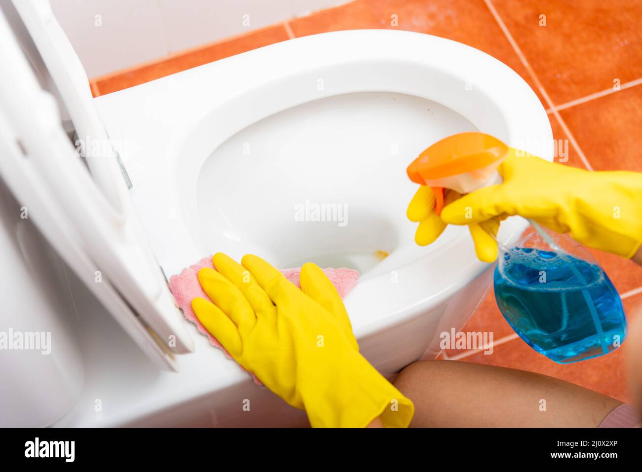 Hand of Asian woman cleaning toilet seat using liquid spray and pink cloth wipe restroom at